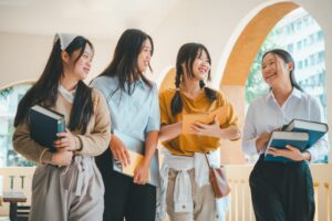 Four young women are walking together, each carrying a book