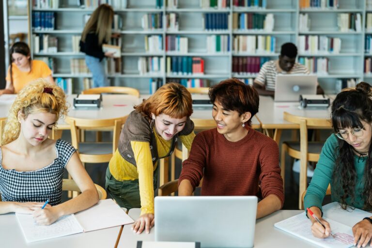 Young university students using laptop and studying with books in library - School education concept