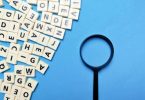 Square letter tiles with magnifying glass against blue background.